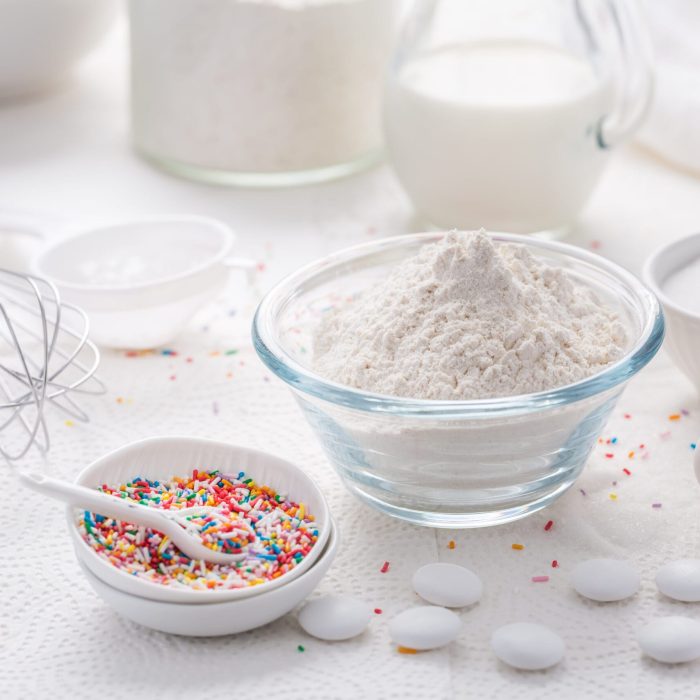 Baking background with flour, eggs, sugar sprinkles, kitchen tools, utensils in white